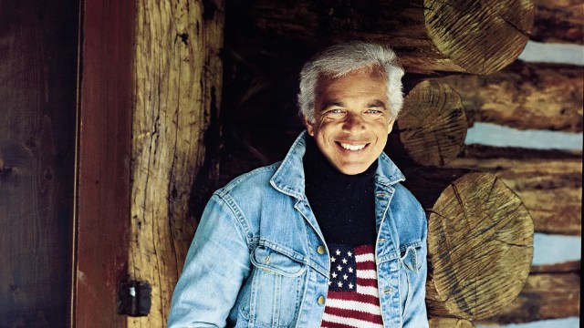 Ralph Lauren smiling, wearing a denim jacket and a flag sweater